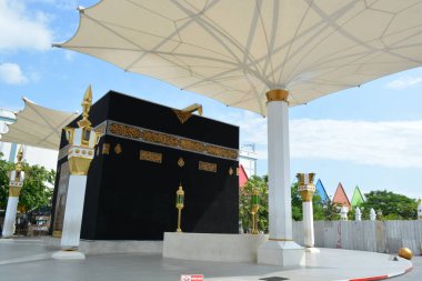 15 Haziran 2025 'te Madiun Endonezya' nın büyük kumaş gölge şemsiyeleri ve dekoratif sütunlarının altındaki Kabe kopyasını gösteren geniş bir kompozisyon.
