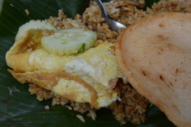 Endonezya Nasi Goreng 'i katlanmış yumurta omleti dilimlenmiş salatalık ve muz yaprağında gevrek kraker ile servis edilir.