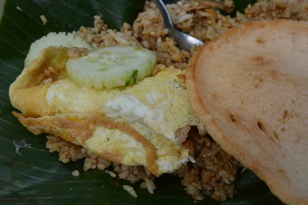 Endonezya Nasi Goreng 'i katlanmış yumurta omleti dilimlenmiş salatalık ve muz yaprağında gevrek kraker ile servis edilir.