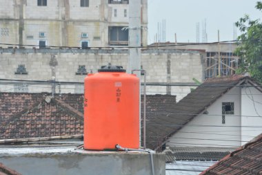 Kediri Endonezya kentsel yapı arka planına sahip bir çatı katına yerleştirilen turuncu plastik su tankı, 10 Şubat 2026 kamu hizmetleri altyapı temizliği ve kentsel gelişimi temaları için kullanışlıdır..