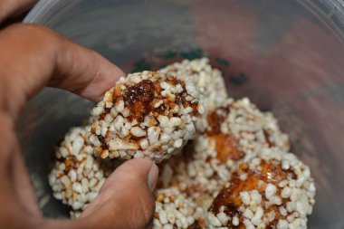 Bir konteynırın üzerinde tek bir pirinç topunu tutan bir elin yakın görüntüsü. Çıtır pirinç ve yapışkan şurubun keskin ayrıntıları servis ve porsiyon seçim temaları ile uyuşuyor.