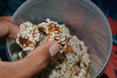 Parmaklar, şişirilmiş pirinç topunu benzer şeylerle dolu bir küvetin üzerine kaldırır. Sahne, atıştırma saati bölümünü ve yaşam tarzı ve gıda pazarlaması için seçilmiş temaları içeriyor.