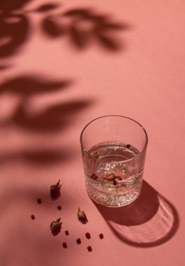 Cin, tonik ve gül tomurcuklarıyla süslenmiş kristal bardak ve pastel pembe arka planda kırmızı biber. Olay yerinin üzerine gölge koy. Minimum yaz içeceği konsepti.