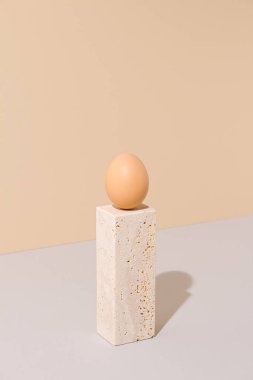 Tek yumurta bej ve gri arka planda travertin mermer bir blokta duruyor. 2021 Paskalya benzersiz natürmort yaşam kompozisyonu. Gerçeküstü yaratıcı organik gıda konsepti.