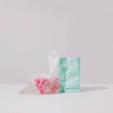 Gri arkaplanda mavi seramik vazoya yaslanmış suyla dolu plastik bir buzdolabı poşetinde pembe şakayık çiçekleri. Gerçeküstü sanat yönetmenliği çiçekli natürmort. Soyut gül çiçeği konsepti.