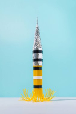 Mavi gökyüzü arka planına karşı spagetti ve alüminyum folyo fırlatma roketi. Soyut 2021 uzay yarışı konsepti. Gerçeküstü uzay yolculuğu fikri.