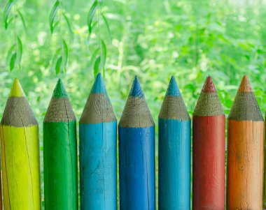 Keskinleştirilmiş renkli kalemler şeklinde çitler yeşil ağaçların arka planına karşı, parlak arkaplan