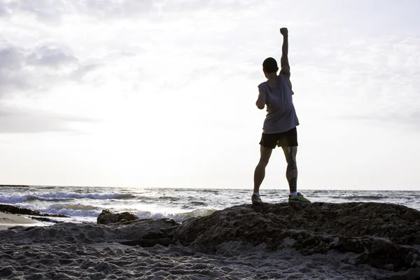 Sportos férfi be a levegő ököl napkelte a strandon — Stock Fotó