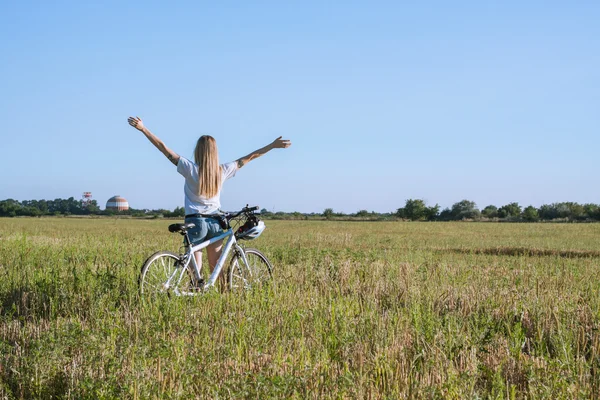 Молода жінка з велосипедом, що піднімається руками на полях — стокове фото