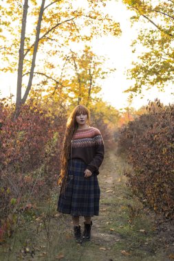 Kızıl saçlı genç bir kadın ve güzel sonbahar ormanlarında süveter giyiyor.