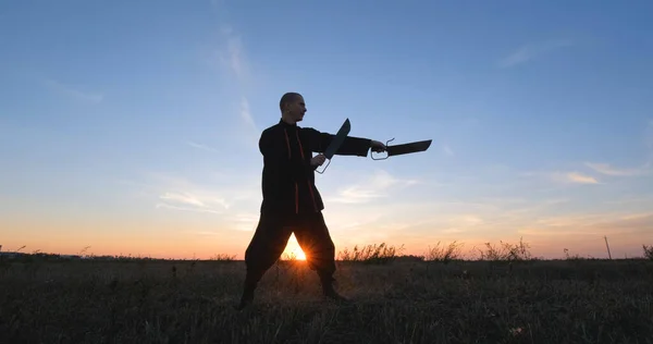 Silhouette of young male kung fu fighter practising alone in the fields during sunset