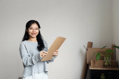 Yeni eve ya da daireye taşınırken elinde panoyla gülümseyen genç bir kadın.
