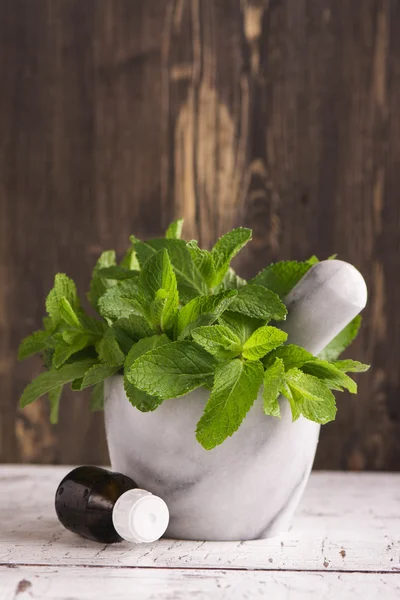 Peppermint oil and fresh mint leaves over wooden table — Stock Photo, Image