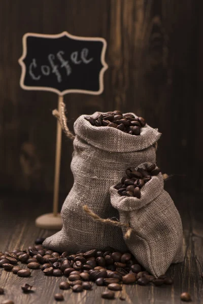 Koffiebonen in jute zakken over houten achtergrond — Stockfoto