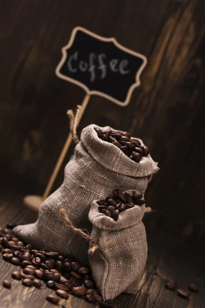Kaffebönor i säckväv säckar över trä bakgrund — Stockfoto
