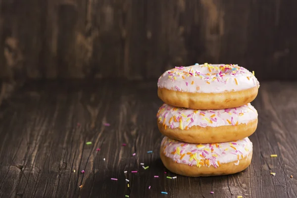 Três donuts doces frescos sobre mesa de madeira — Fotografia de Stock