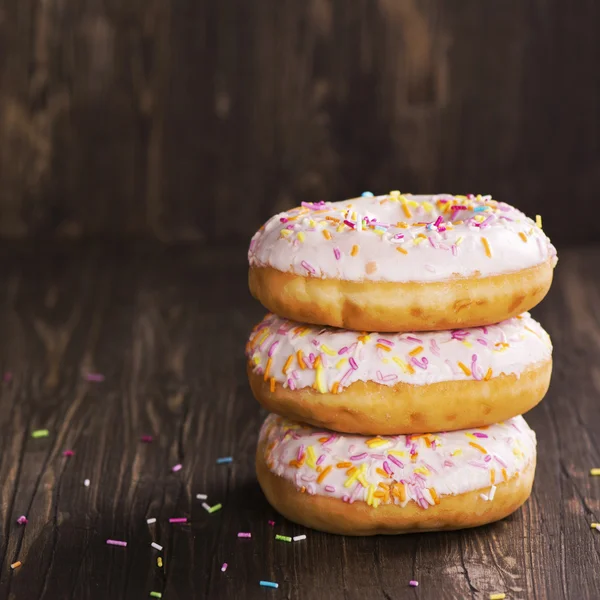 Três donuts doces frescos sobre mesa de madeira — Fotografia de Stock