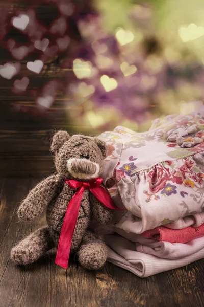 Pilha de roupas de bebê com um urso de pelúcia — Fotografia de Stock