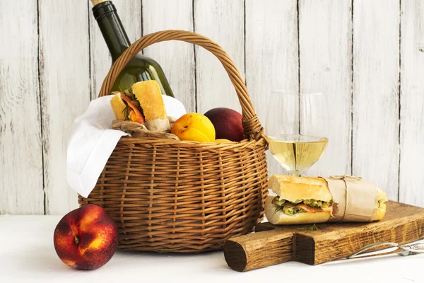 Cesta de picnic con vino, sándwiches de salmón y frutas sobre blanco — Foto de Stock