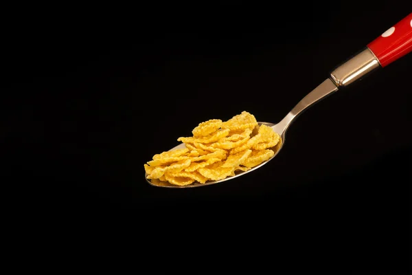 Fiocchi di mais in un cucchiaio su sfondo nero — Foto Stock