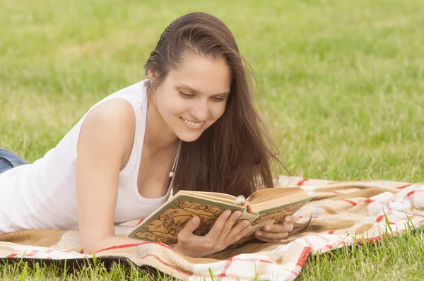 Усміхнена дівчина читає книгу на відкритому повітрі — стокове фото