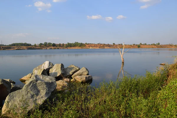 Lago rochoso com pedra e árvore morta — Fotografia de Stock