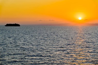 Ufkun üzerinde turuncu bir günbatımı gökyüzü boyunca denizde bir yolcu gemisinin silueti.