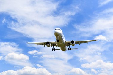 Yolcu uçağı beyaz bulutlu mavi gökyüzünün altında havaalanına iniyor.