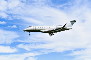 Mavi gökyüzünün altında beyaz bulutlarla uçan özel bir iş uçağı.