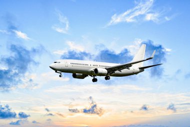 Yolcu uçağı turuncu bir günbatımı gökyüzünün altında havaalanına iniyor.