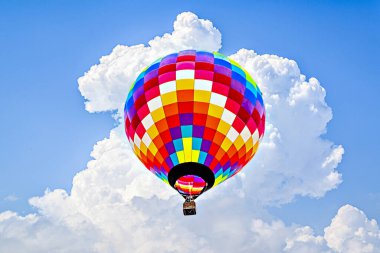 Mavi gökyüzünde beyaz bulutlarla uçan renkli sıcak hava balonu