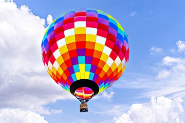 Mavi gökyüzünde beyaz bulutlarla uçan renkli sıcak hava balonu
