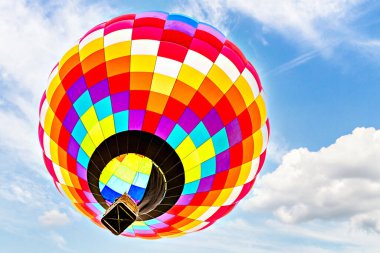 Mavi gökyüzünde beyaz bulutlarla uçan renkli sıcak hava balonu