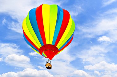 Mavi gökyüzünde beyaz bulutlarla uçan renkli sıcak hava balonu