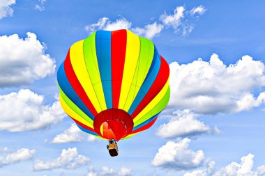 Mavi gökyüzünde beyaz bulutlarla uçan renkli sıcak hava balonu