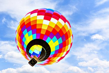 Mavi gökyüzünde beyaz bulutlarla uçan renkli sıcak hava balonu