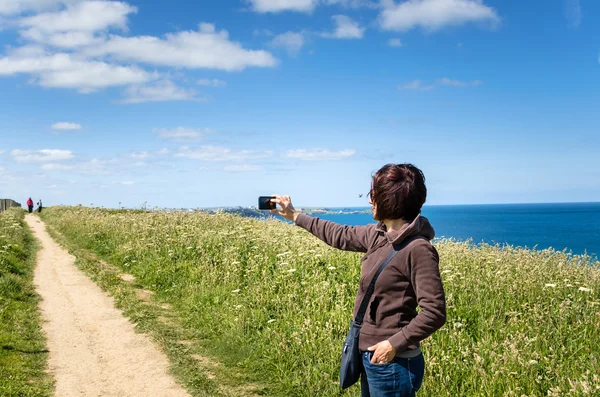 Mujer joven tomando fotos con su teléfono móvil en un camino de acantilado — Foto de Stock