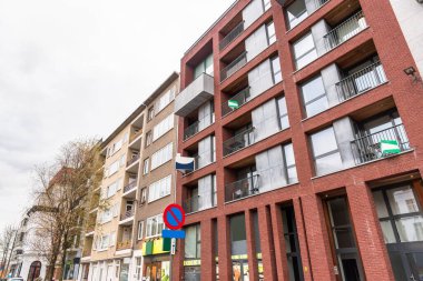 Bulutlu bir günde zemin katlarında dükkanları olan modern apartmanlar. Bazı dairelerin balkonlarında kiralık olduklarını gösteren emlak tabelaları asılı. Antwerp, Belçika.