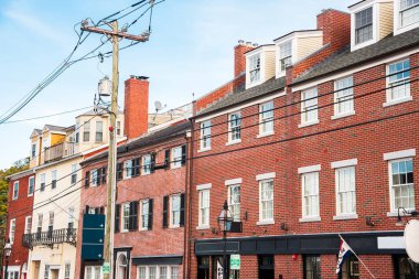 Gün batımında şehir merkezinde zemin katta dükkanları olan geleneksel tuğla binalar. Önplanda trafoya ve kablolara sahip bir elektrik direği görülüyor. Portsmouth, NH, ABD.