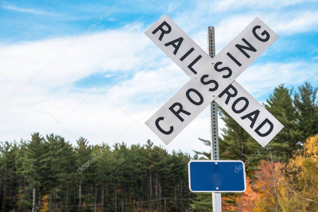 Railroad crossing sign with trees in background and blue sky with clouds. Copy space.