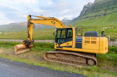 Parçalı bulutlu bir yaz gününde İzlanda 'da bir dağ yolunda bir inşaat alanında kazıcı.