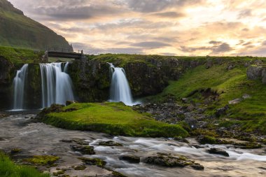 Gün batımında güzel bir şelalenin üzerinde küçük bir köprü. Kirkjulsfoss, İzlanda.