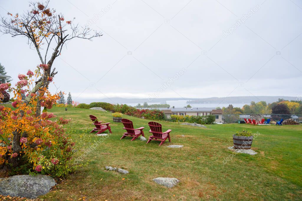 Wooden Adirondack chairs in lawn overlooking a lake on a foggy autumn day. Lakes region, NH, USA.