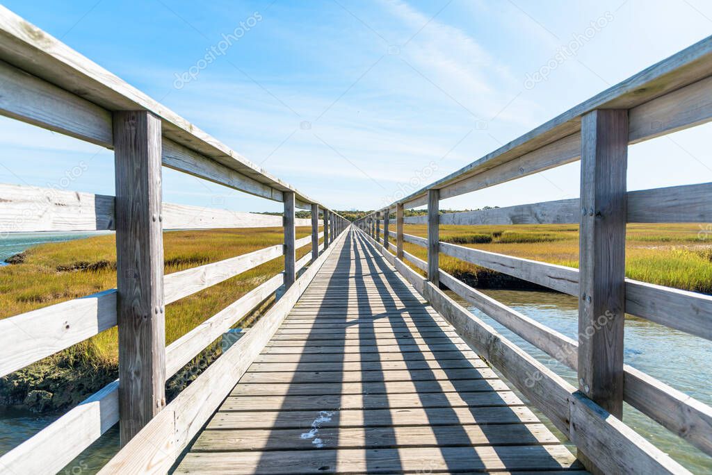 View of a deserted straight fenced walkway through a saltwater mashland on a clear autumn day. Converging lines. Cape Cod, MA, USA.