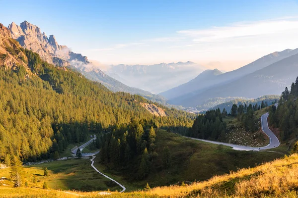 Gün batımında ormanlık bir vadiye giden dolambaçlı bir dağ yolu. Sonbaharda Avrupa Alplerinde görkemli dağ manzarası.