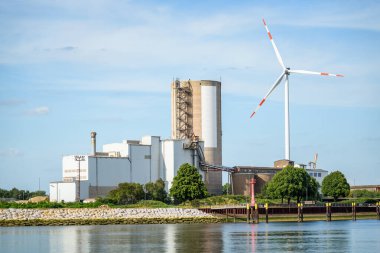 Sanayi fabrikası ve rüzgar türbini güneşli bir yaz gününde nehir kenarındaki ticari bir rıhtımda. Bremen, Almanya.