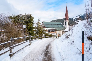 Tyrol 'daki bir dağ köyünde kışın karla kaplı bir patika bulundu. Arka planda uzun çan kulesi olan geleneksel bir kilise görülebilir. Seefeld, Avusturya.