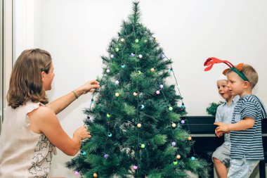 Anne ve iki küçük çocuk Noel ağacı süslüyorlar.