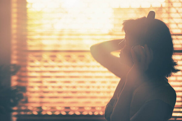 A silhouette of woman with Headphone or Headset on her head with the window and sunlight on background.