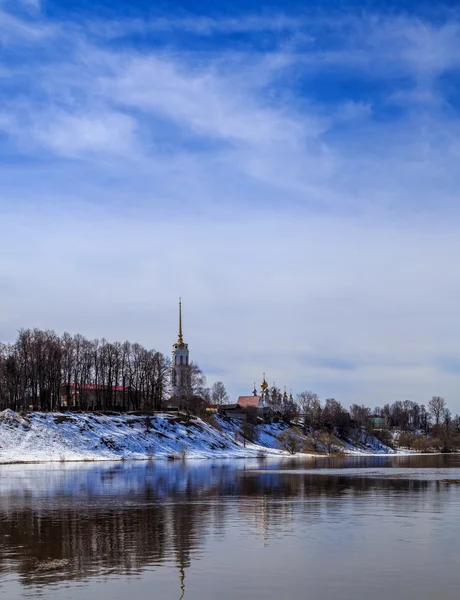 De rivier overstroomd, de banken nog steeds sneeuw, blauwe hemel met licht wolken — Stockfoto